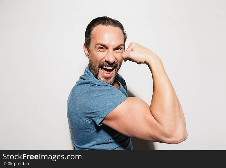 Portrait of a happy mature man dressed in t-shirt showing biceps isolated over white background