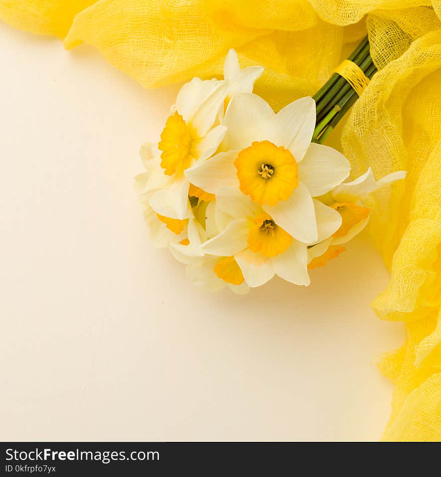 White daffodil bouquet with yellow textile decoration on pastel background with copy space.