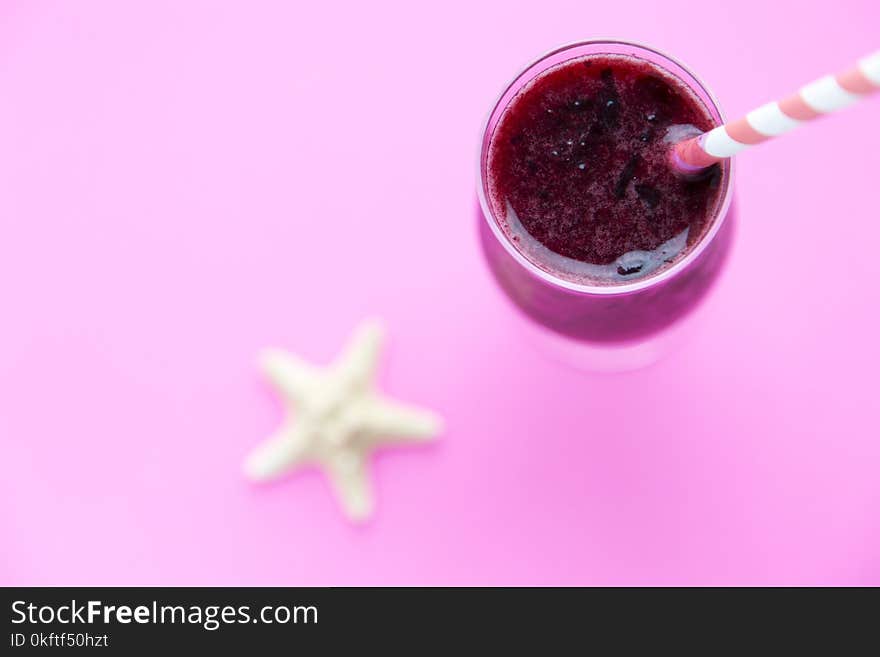 Glass of black currant milkshake or cocktail on pink background.