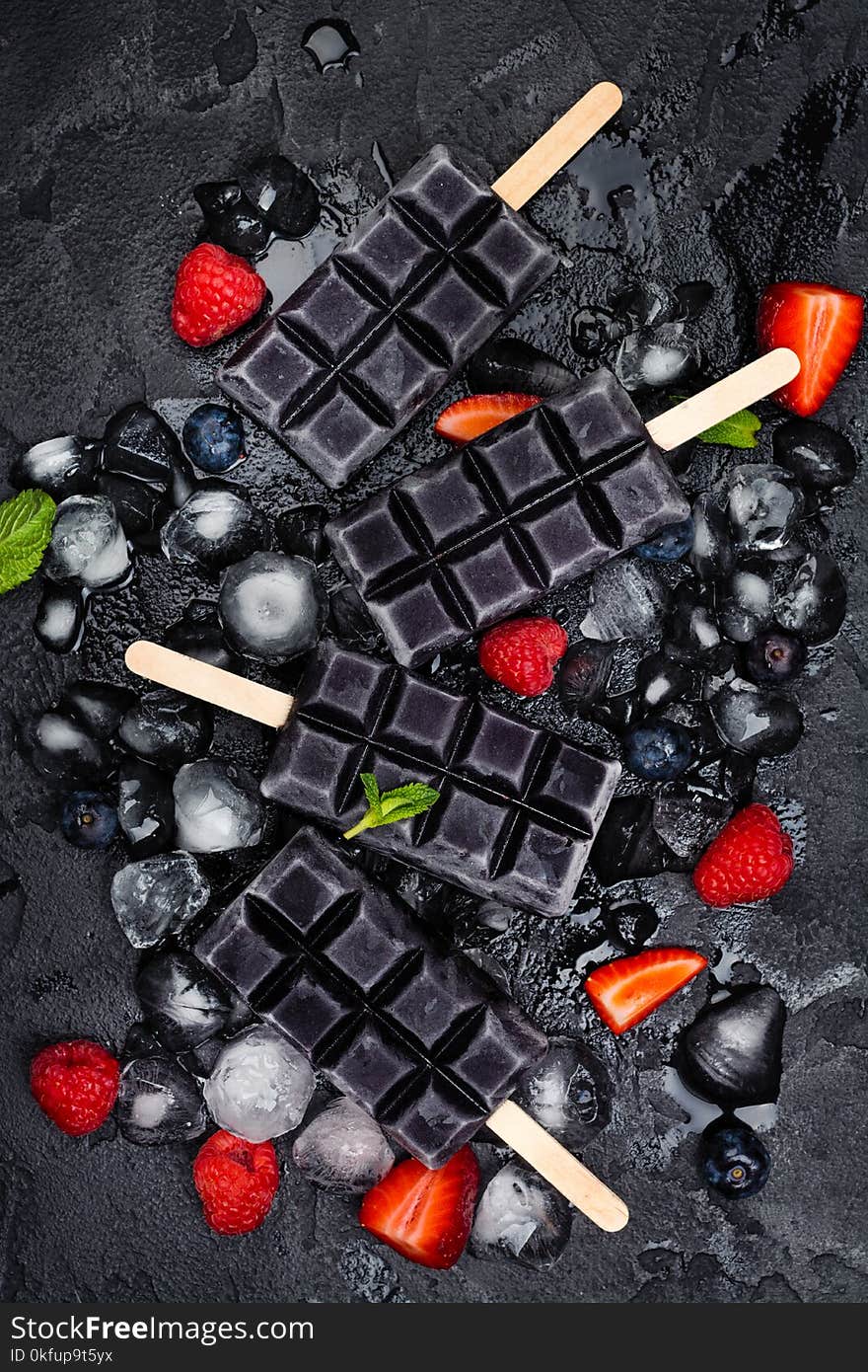 Trendy black charcoal ice cream popsicles with berries on stone background. Copy space