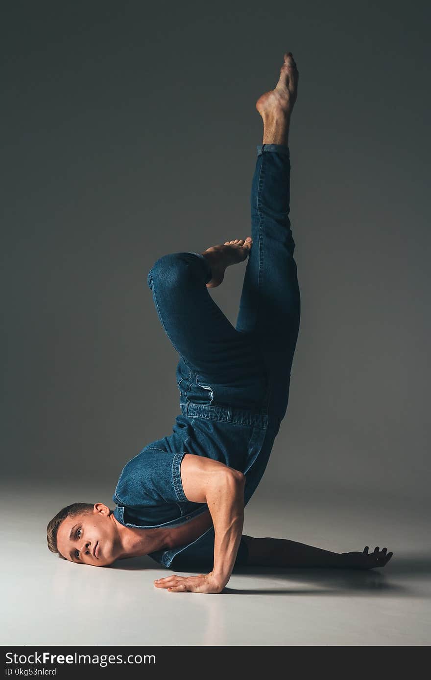 the guy is dancing, the pose of the leg is up, face to the floor, hands are lying on the floor, on a faded background in a denim s