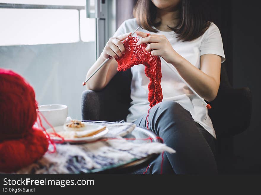 Close up shot of young woman hands knitting a red scarf handicraft in the living room on terrace at home.