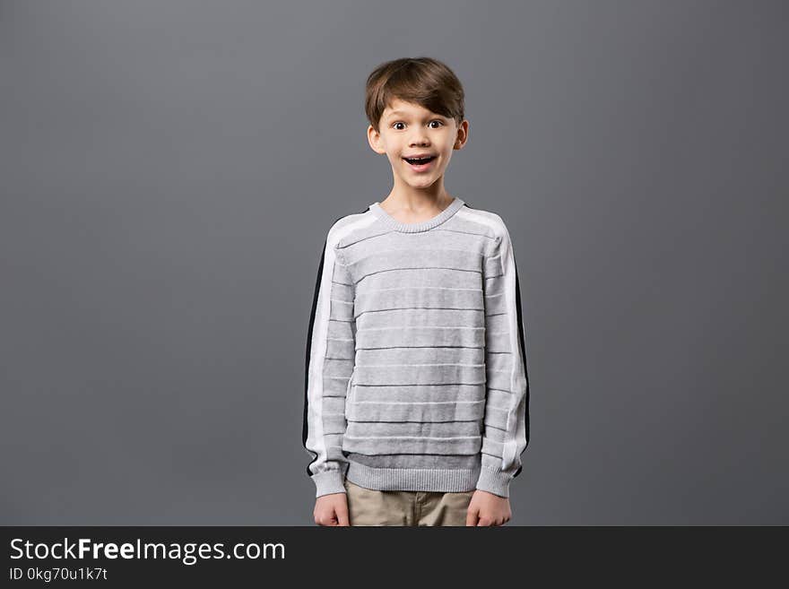 Emotional child. Happy excited boy standing against grey background and looking at you. Emotional child. Happy excited boy standing against grey background and looking at you