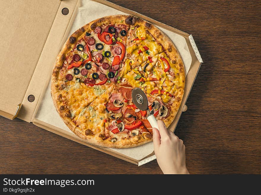 The girl`s hands cut a huge pizza in a box. Four pizzas in one