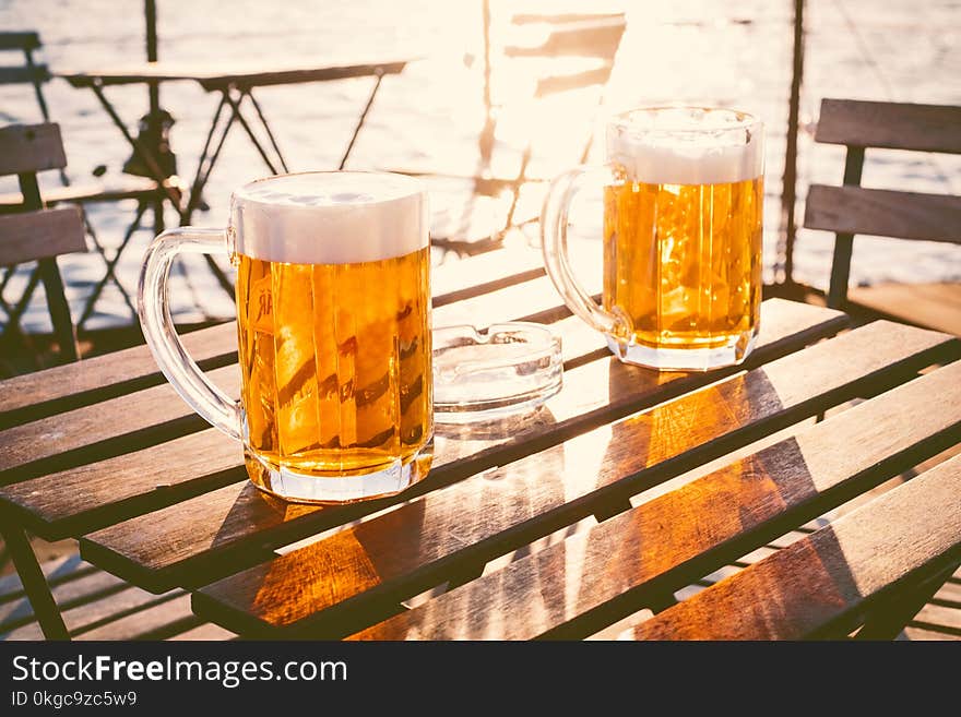 Two glasses of light beer with foam on a wooden table.On a boat. Garden party. Natural background. Alcohol. Draft beer. Landscape, golden