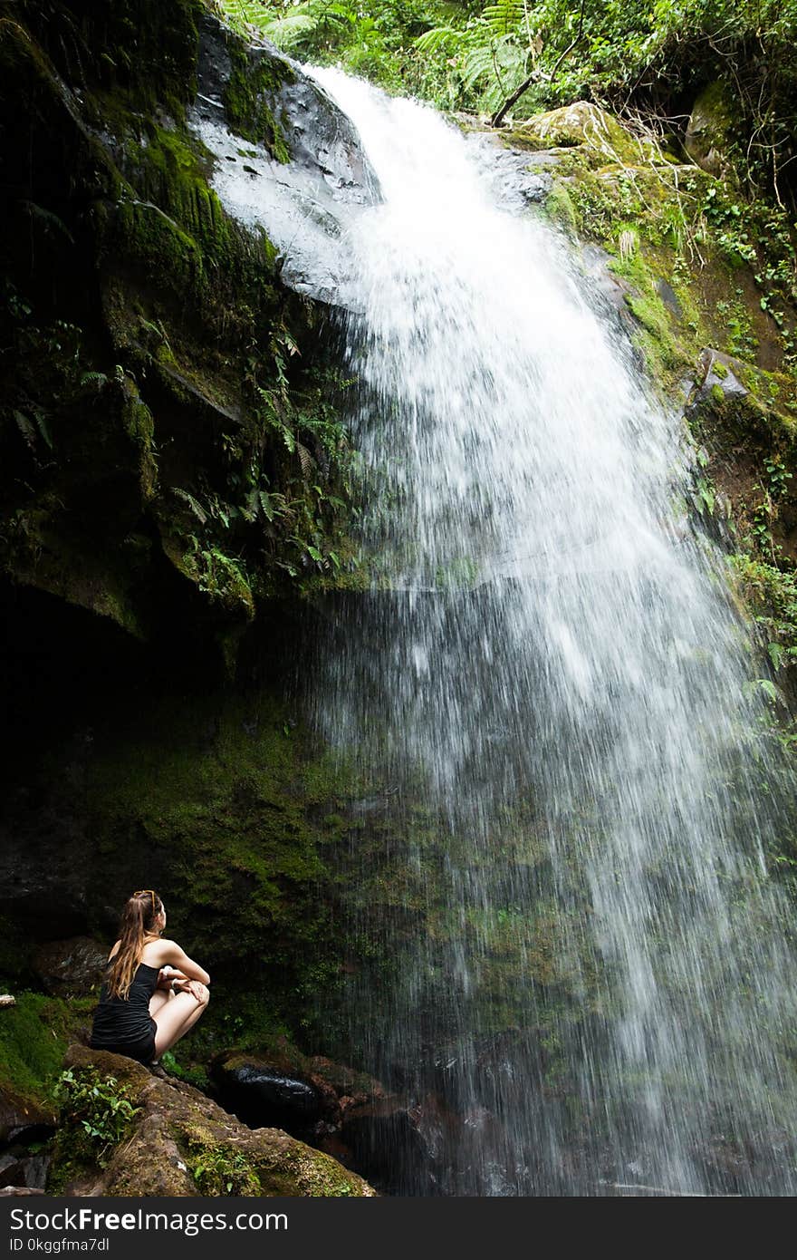 Photo of Woman Sitting on Rock Facing the Waterfalls