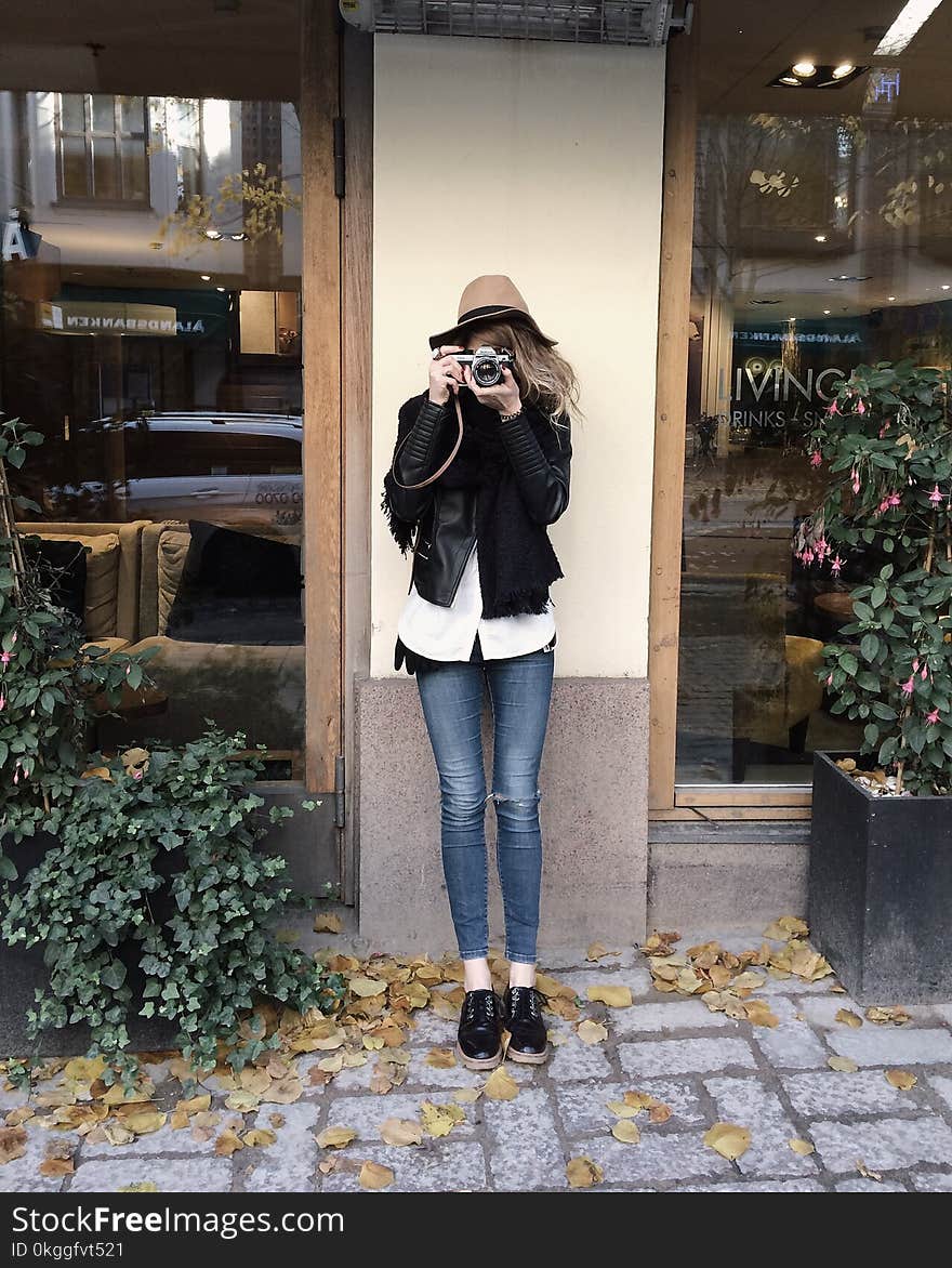 Woman Wearing Black Jacket and Blue Jeans Leaning on Wall