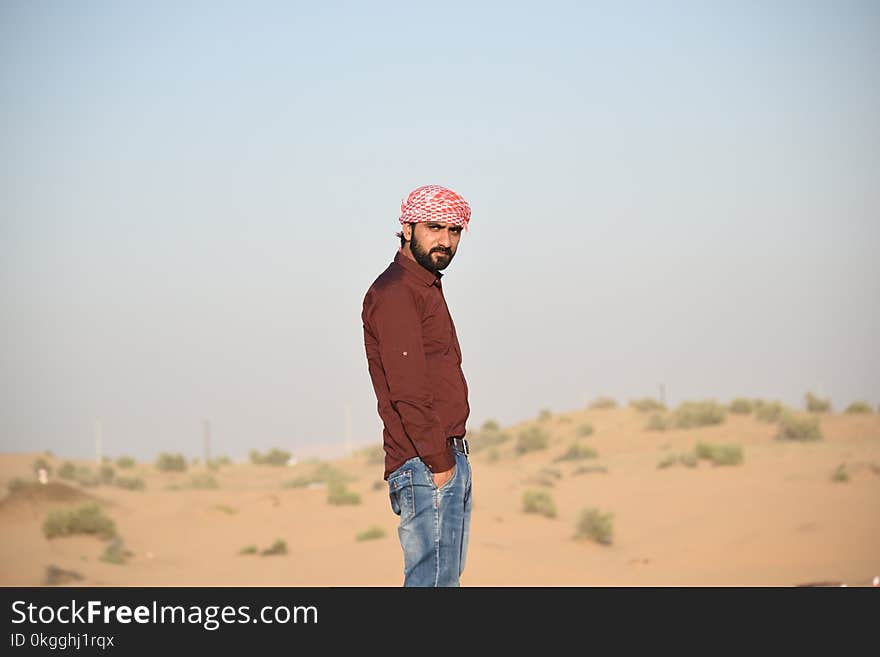 Man in Brown Collared Dress Shirt and Blue Jeans Standing in the Middle of Brown Field