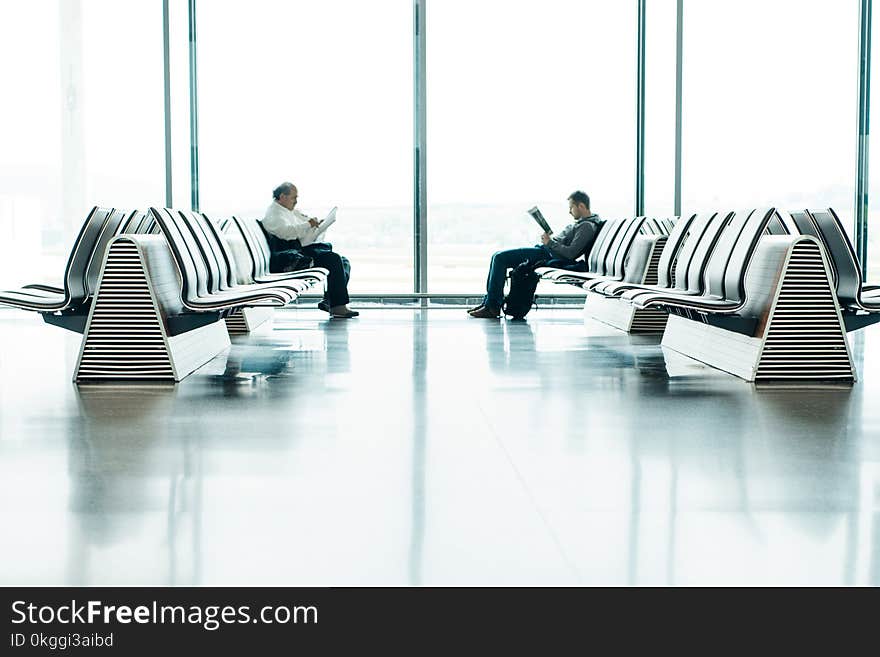 Two Men Sitting in Front of Each Other on White Gang Chairs in Airport Waiting Area