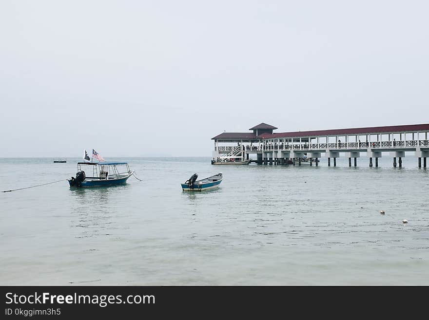 White and Blue Boat on Body of Water Near Pier