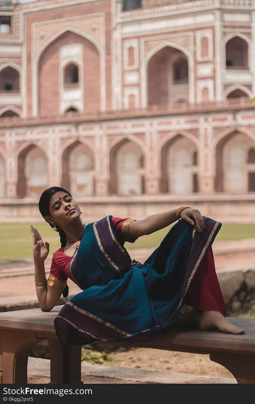 Woman in Blue, Red, and Purple Saree Dress Lying on Bench