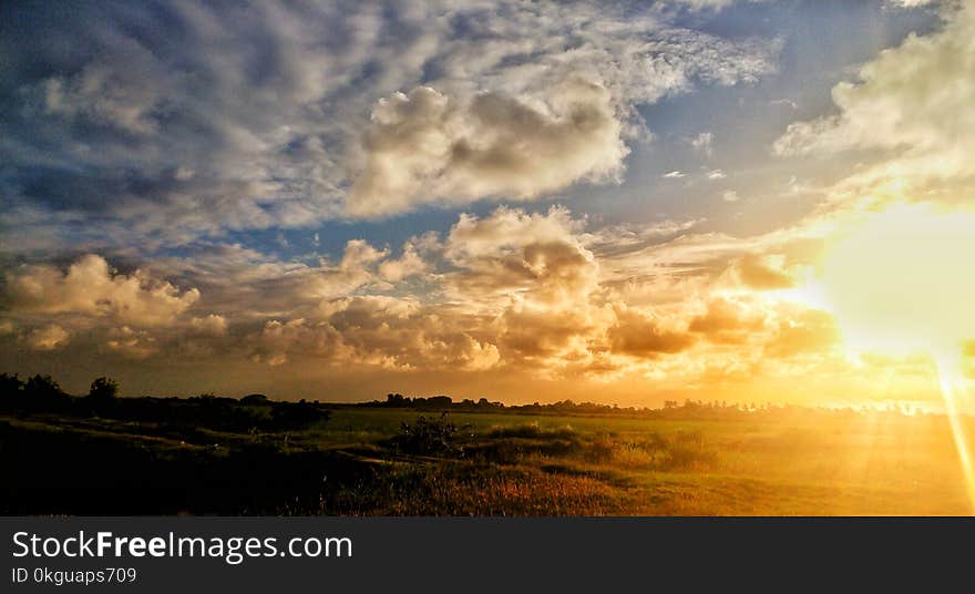 Green Grass Field Under Cloudy Sky during Sunset