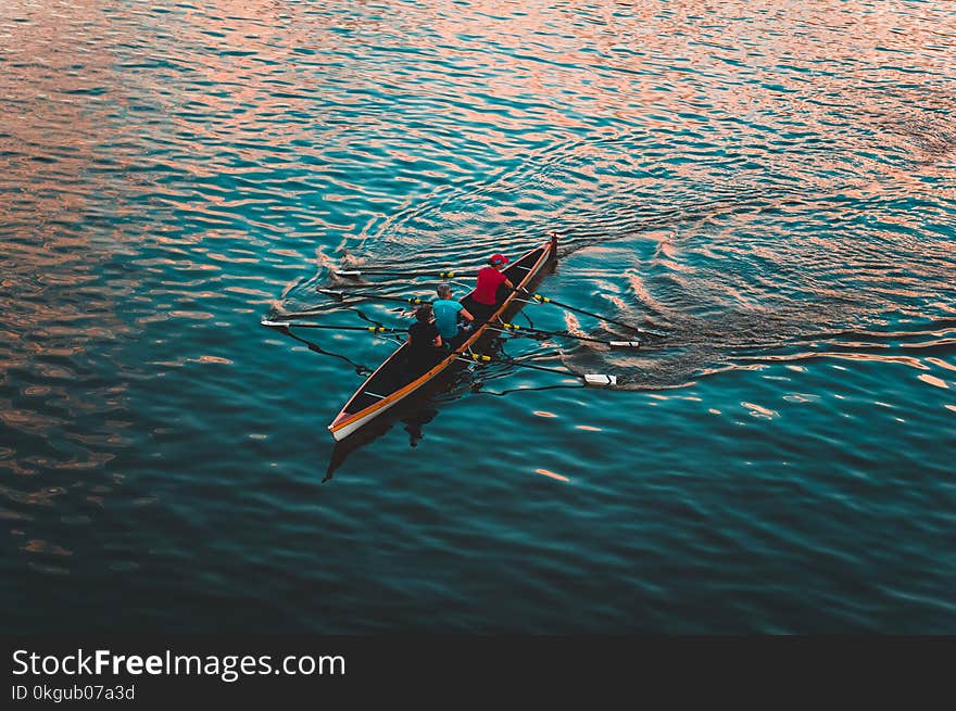 Three People on Brown Canoe Sailing on Calm Water