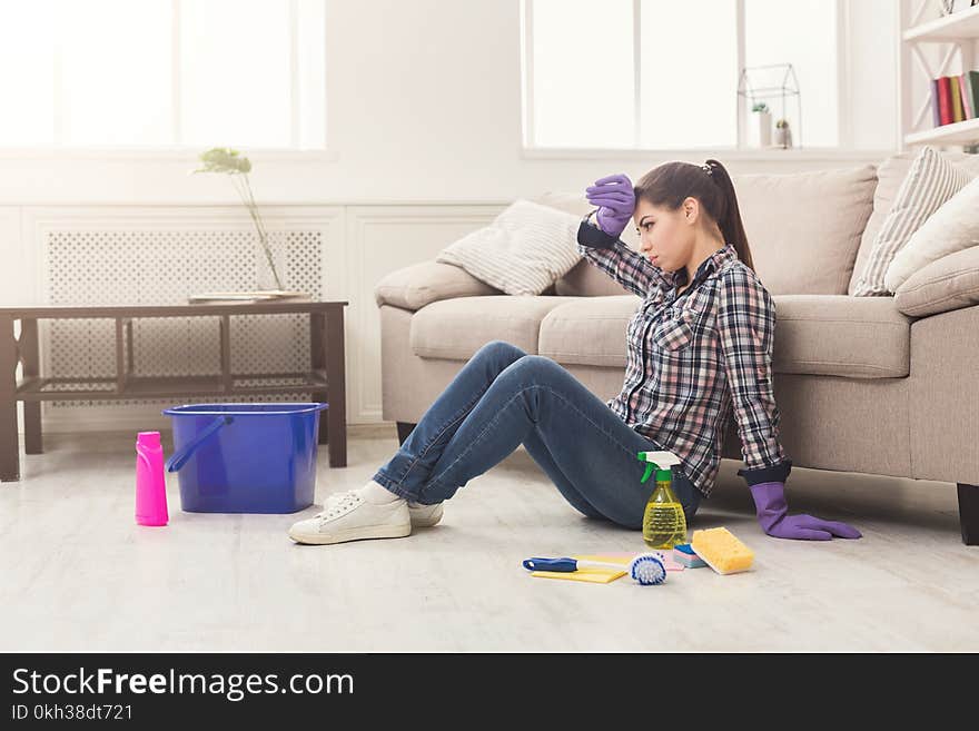 Tired woman cleaning floor with lots of tools. Young tired girl surprised of detergents quantity, copy space