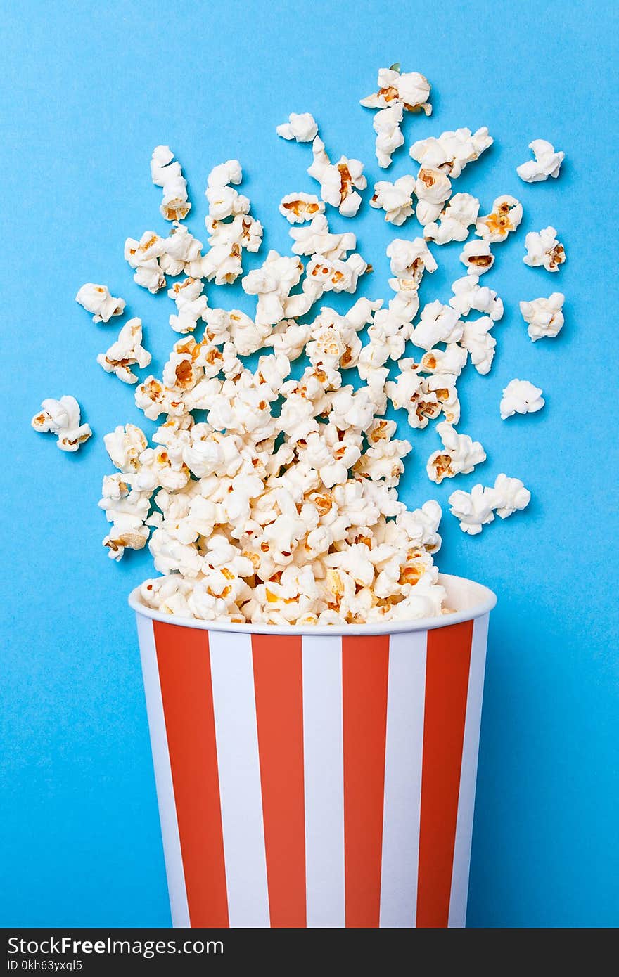 Spilled popcorn and paper bucket in red strip on blue background. Copy space for text.