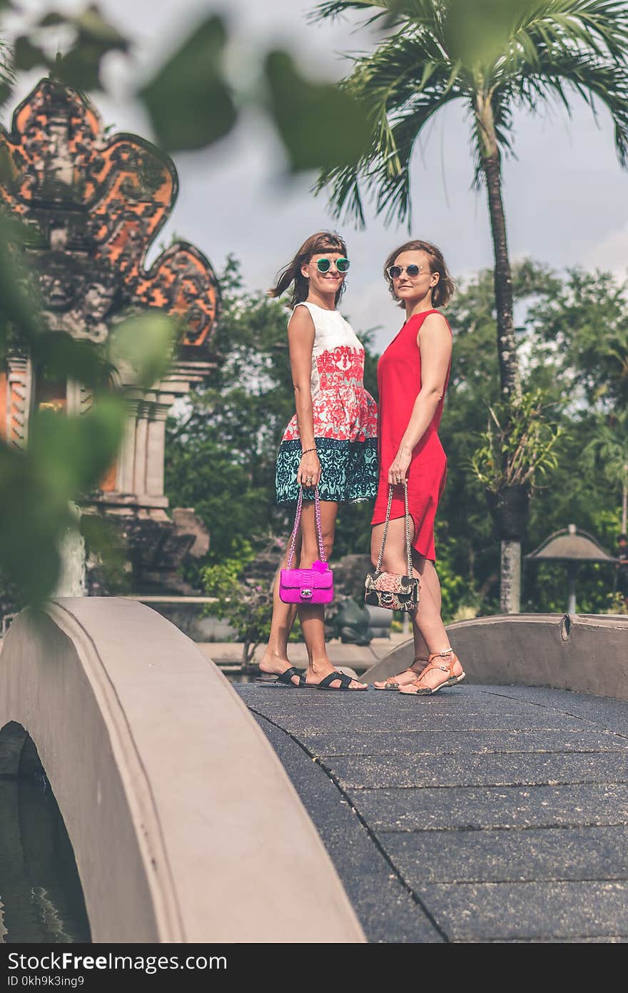 Two Women Wearing Sunglasses and Holding Bags Standing on Foot Bridge