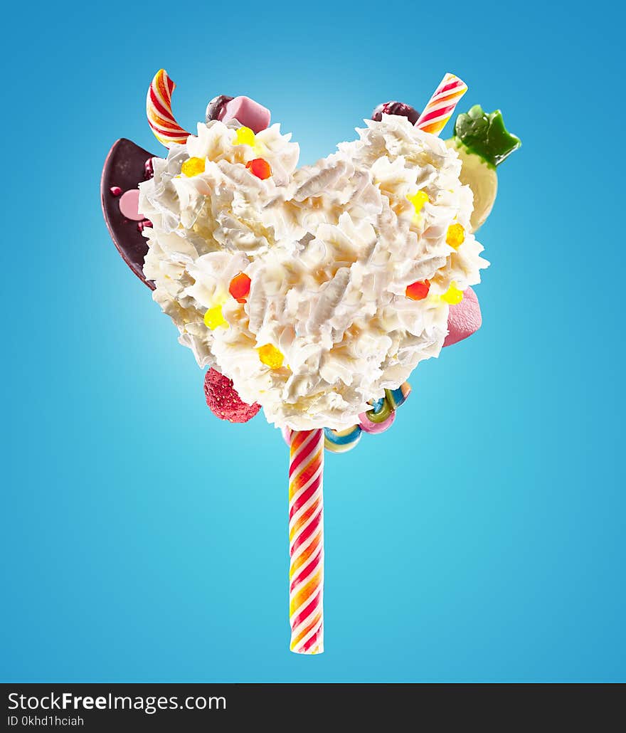 Sweet Lolipop in Heart form of whipped cream with sweets, jellies, heart front view. Crazy freakshake food trend. Front view of whipped heart of cream lolly, full of berry and jelly sweets, chocolate candy. Colored whipped heart form cream concept on color background