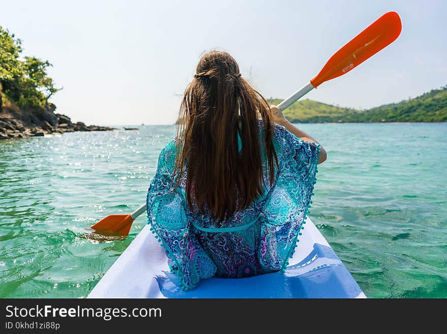 Young Woman Paddling A Canoe Along The Shore Of An Idyllic Island