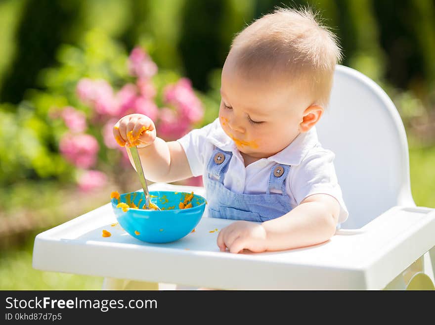 Cute toddler with messy face eating lunch in garden, sitting in