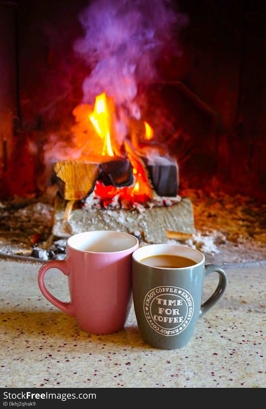 Bright colorful flame, burning wood at the fireplace, two coffee caps. Couple coffee caps, firewood fire on the background.