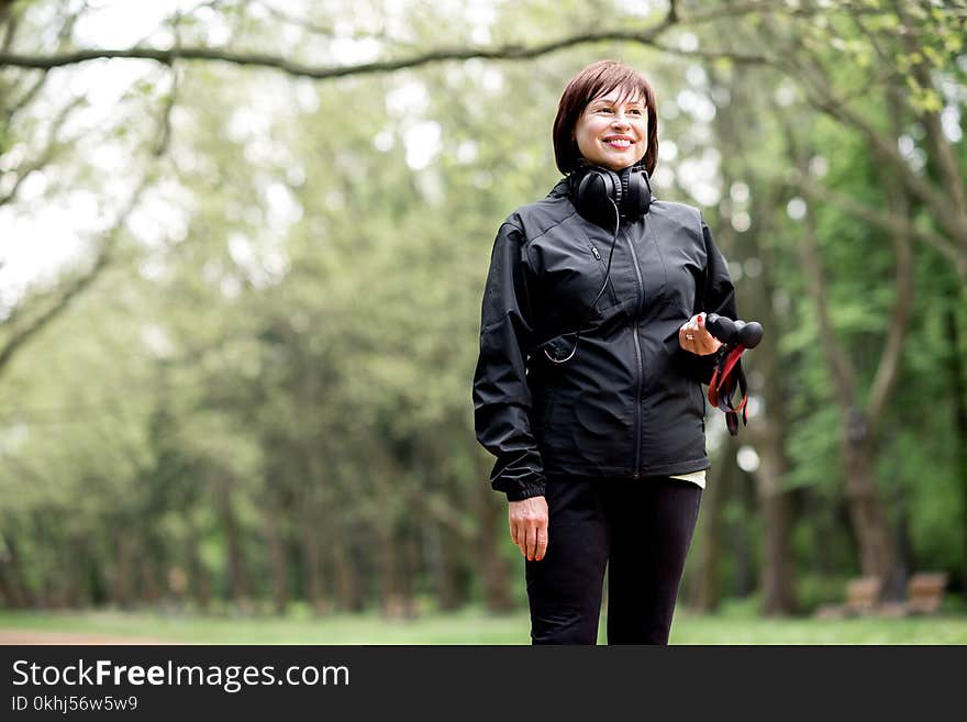 Portrait of an elder woman in black sportswear standing with hiking sticks in the park. Portrait of an elder woman in black sportswear standing with hiking sticks in the park