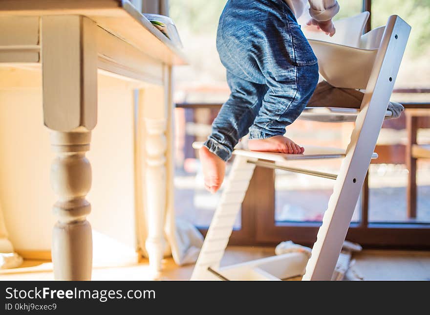 Little toddler boy climbing on wooden highchair at home. Domestic accident. Dangerous situation at home. Little toddler boy climbing on wooden highchair at home. Domestic accident. Dangerous situation at home.