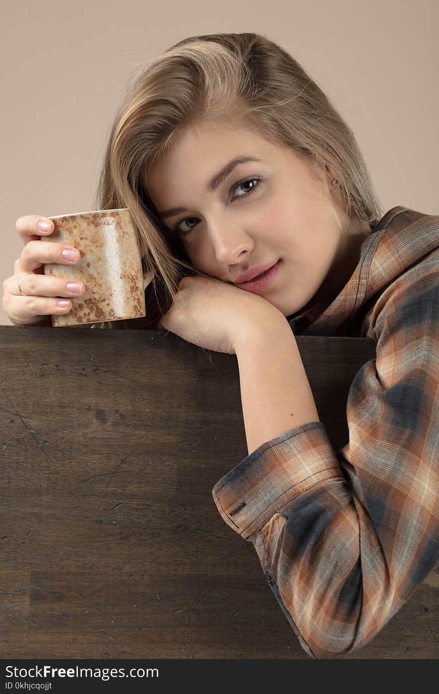 Young pretty blonde woman in brown plaid shirt with coffee mug