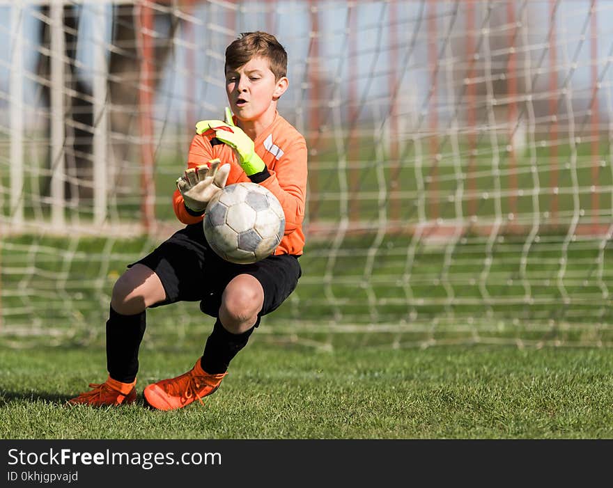 Young Boy Goalkeeper Saving A Football In A Game Of Soccer.