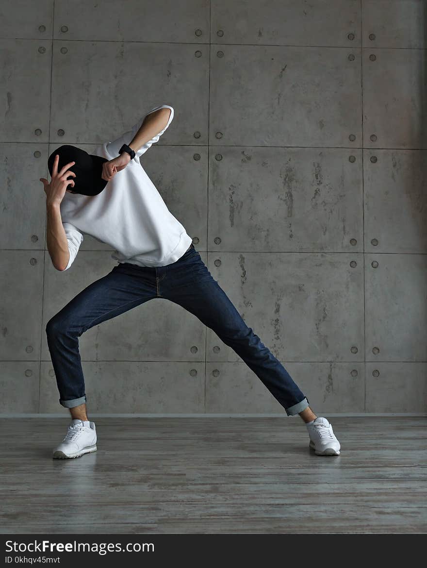 Teenager guy in baseball cap and sneakers, jeans and white sweater dancing hip-hop. Dynamics of modern dance movement. Youth fashion. Man is unrecognizable. Teenager guy in baseball cap and sneakers, jeans and white sweater dancing hip-hop. Dynamics of modern dance movement. Youth fashion. Man is unrecognizable