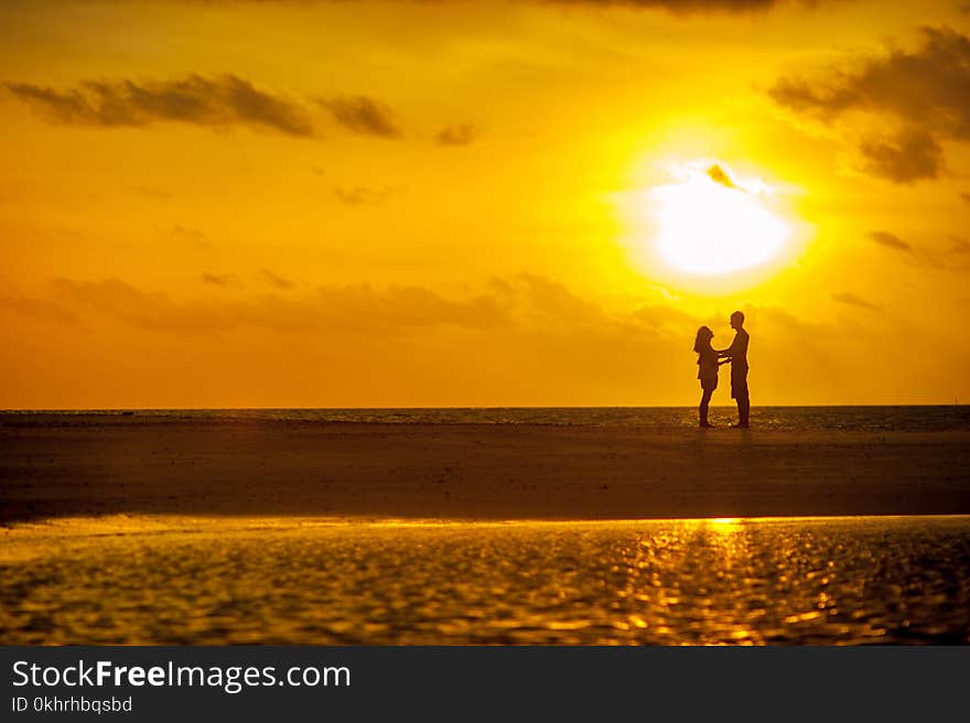 Man and Woman Standing Near Seashore Under Sunset