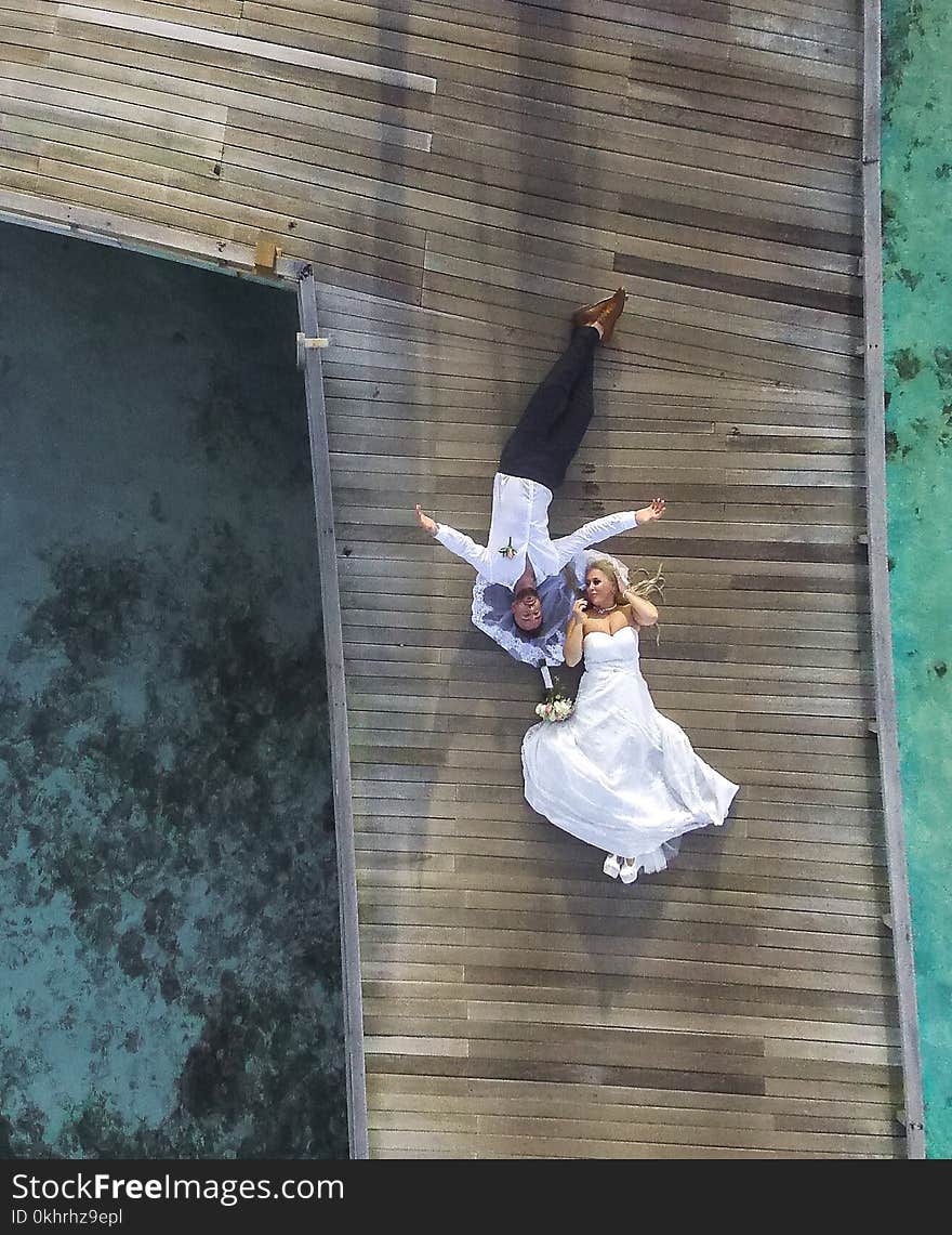 Photo of Bride and Groom Laying on Pier