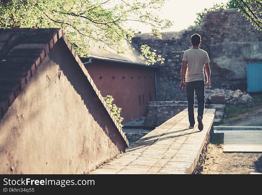 Man Wearing Gray T-shirt and Black Denim Jeans Walking Towards Gray Concrete Pathway