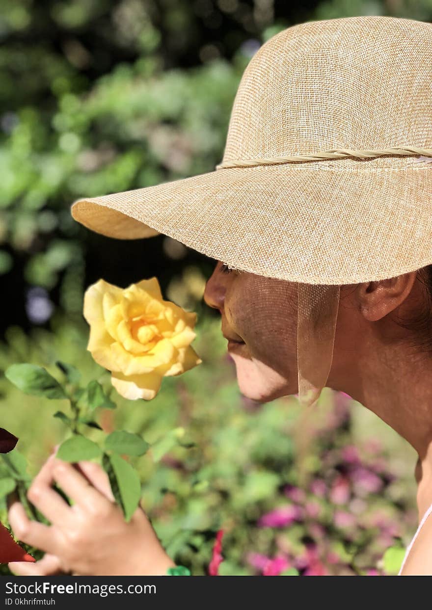 Woman Wearing Sun Hat Smelling Yellow Rose