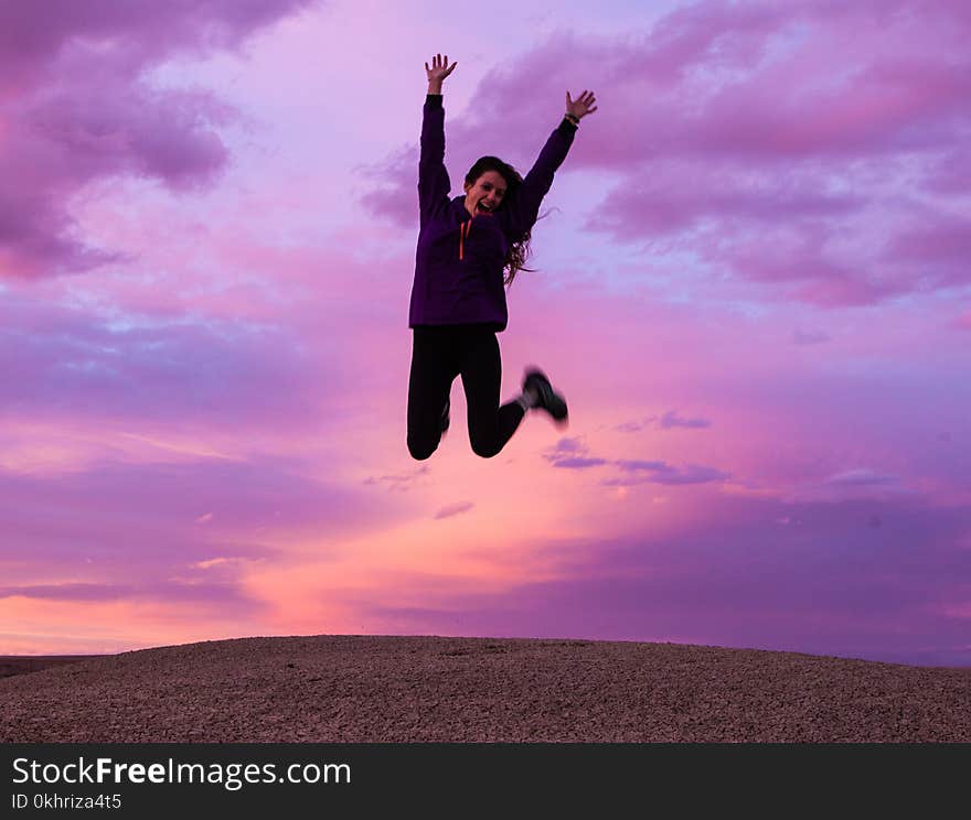 Smiling Woman Wearing Black Jacket and Pants Jumping in Brown Open Field