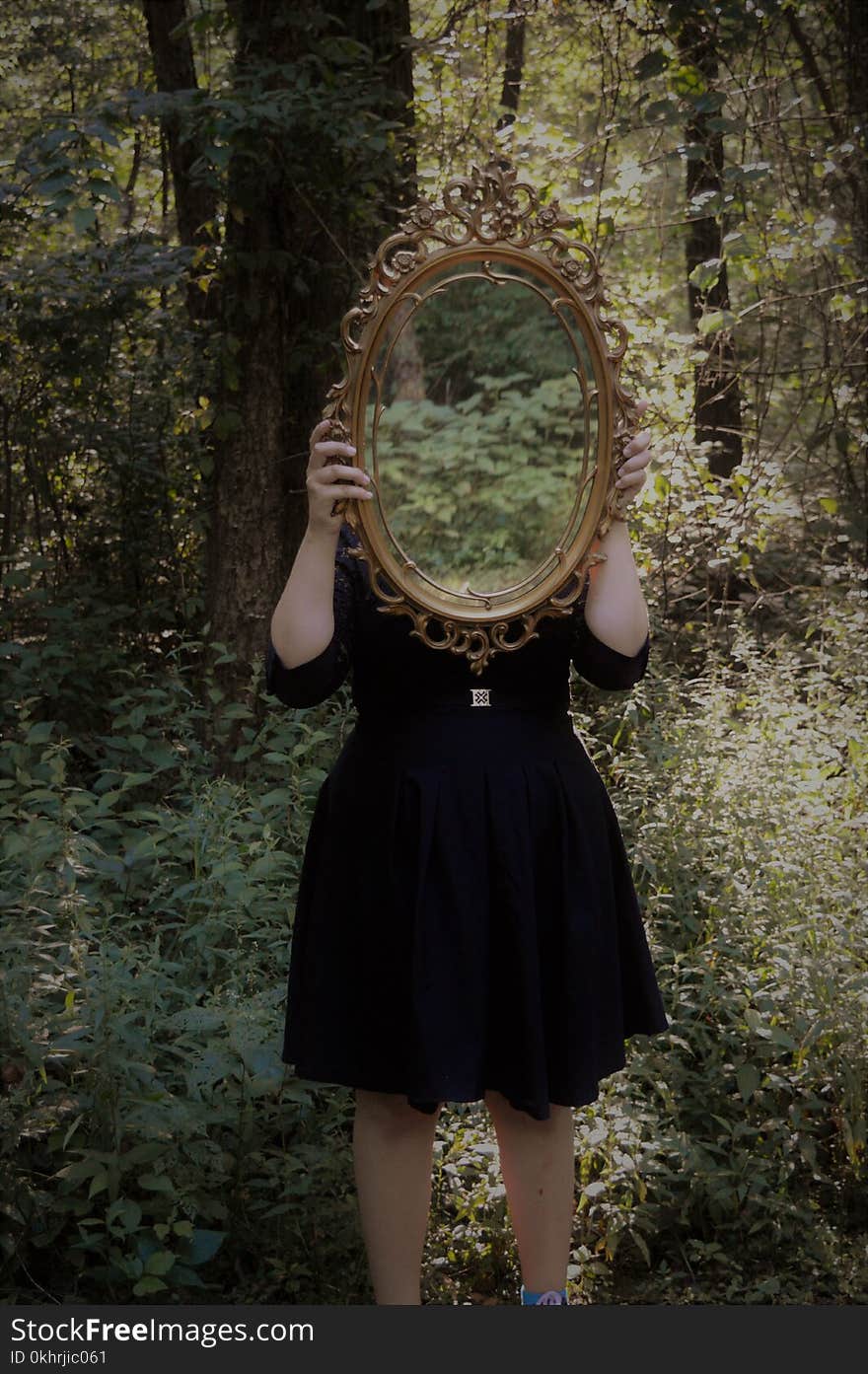 Woman Holding Mirror Against Her Head in the Middle of Forest