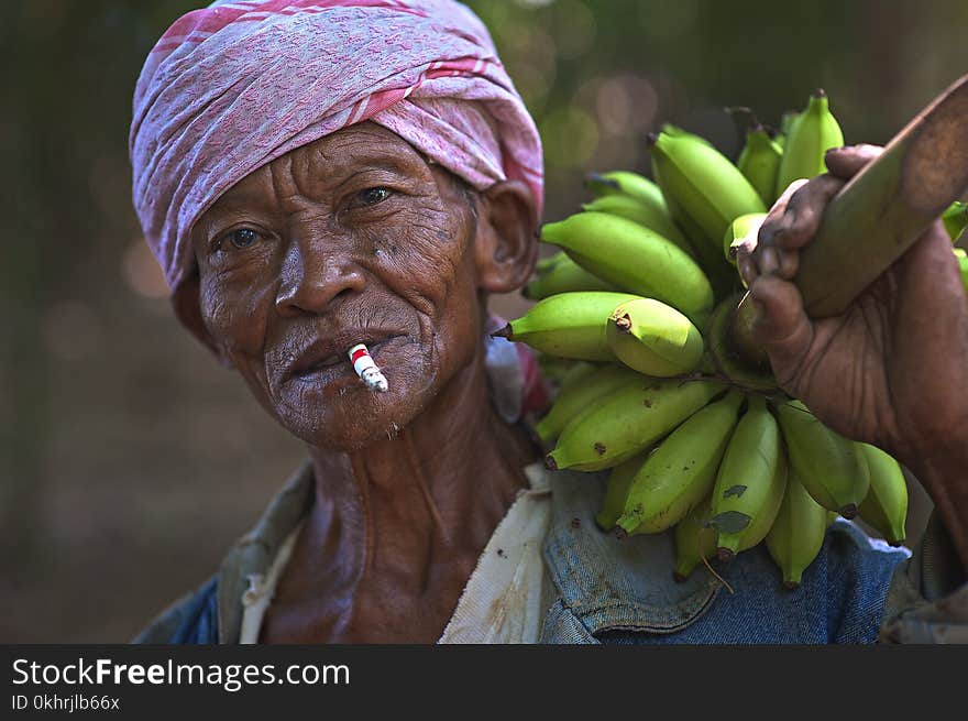 Man Wearing Blue Top Holding Bunch of Unripe Bananas