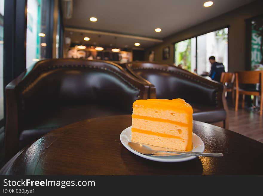 Orange cake on small white dish with spoon on table in coffee shop