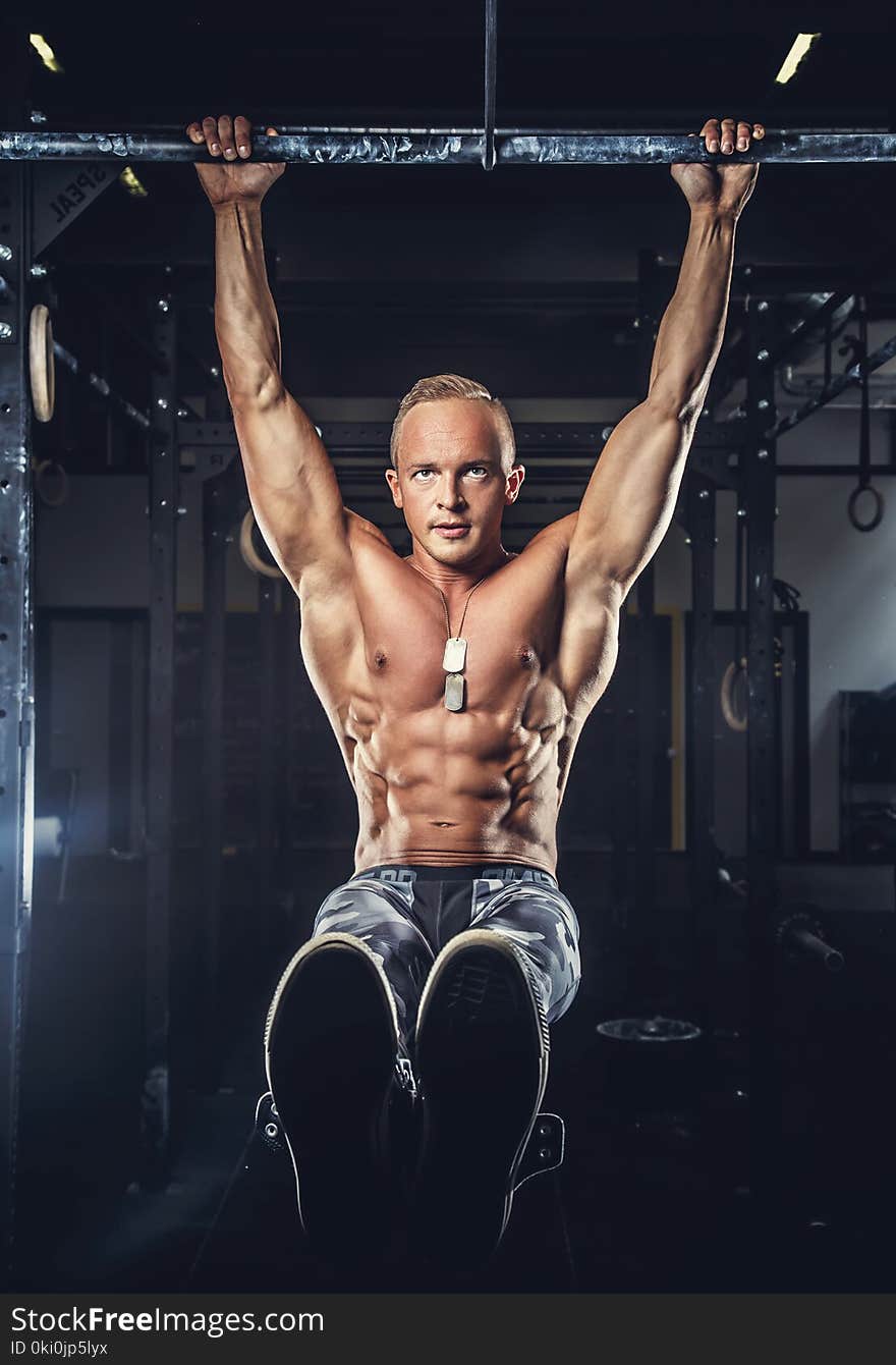 Shirtless muscular man in military pants doing exercises on horizontal bar. Shirtless muscular man in military pants doing exercises on horizontal bar.