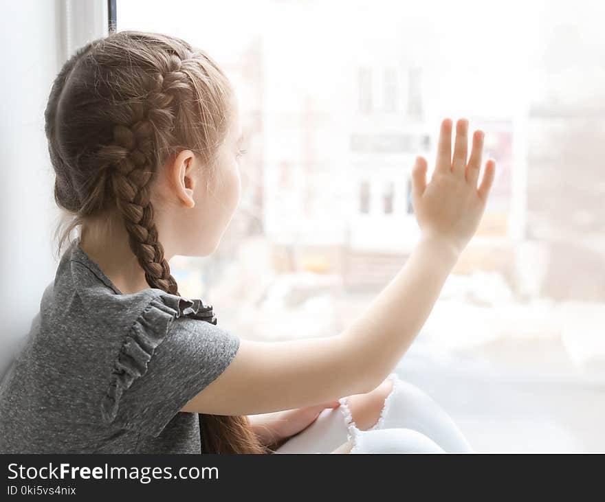 Lonely little girl near window indoors