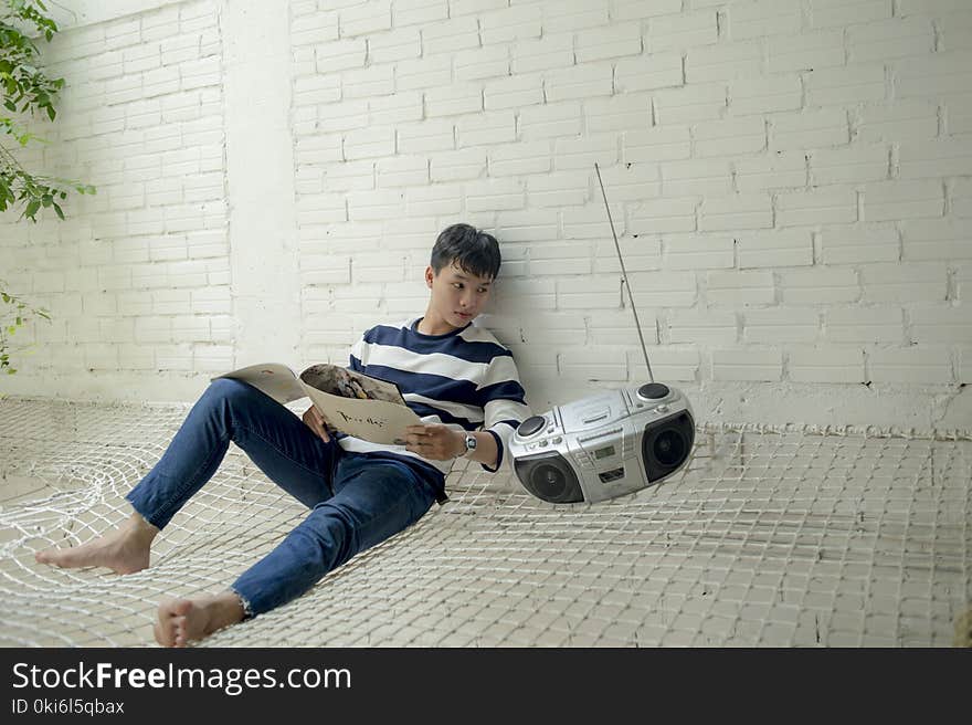 Boy Sitting Near Radio Holding White Catalog