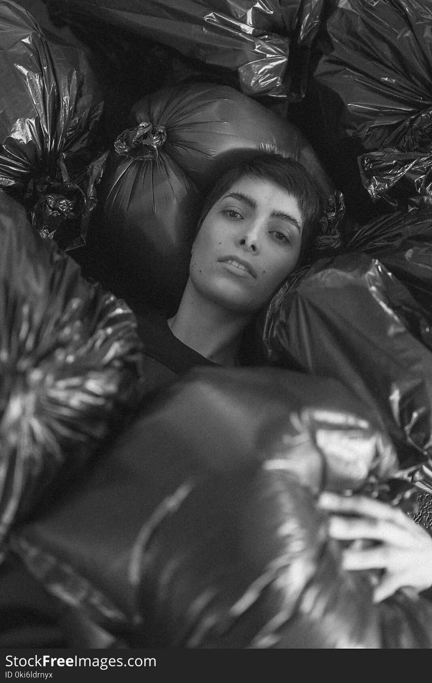 Grayscale Photo of Female Surrounded by Black Plastic Bags