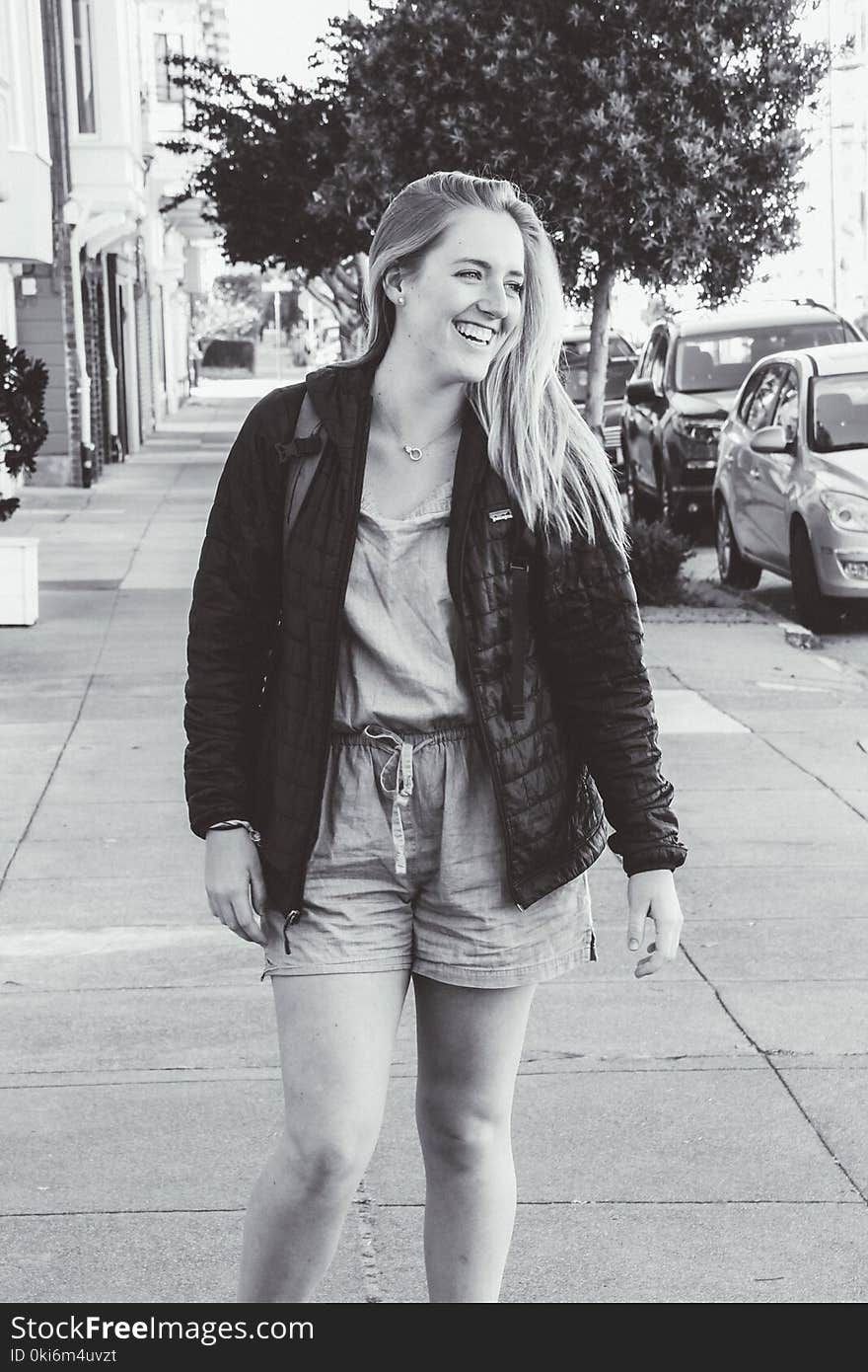 Greyscale Photo of Smiling Woman Wearing Jacket Standing on Pathway