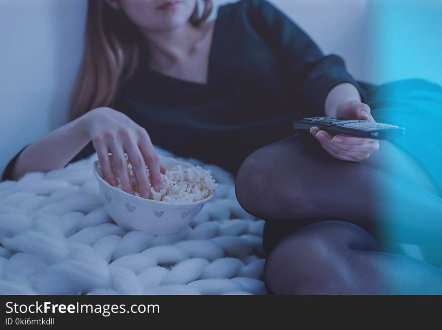 Woman in White Bed Holding Remote Control While Eating Popcorn