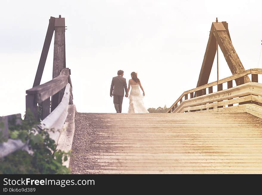 Man and Woman Holding Hands While Walking on Bridge