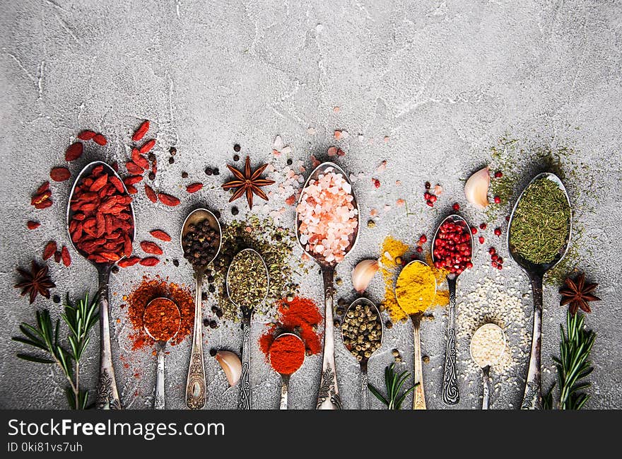 Different kind of spices in vintage spoons on a gray stone background