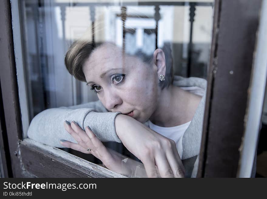 Young attractive unhappy depressed lonely woman looking sad looking through the window at home