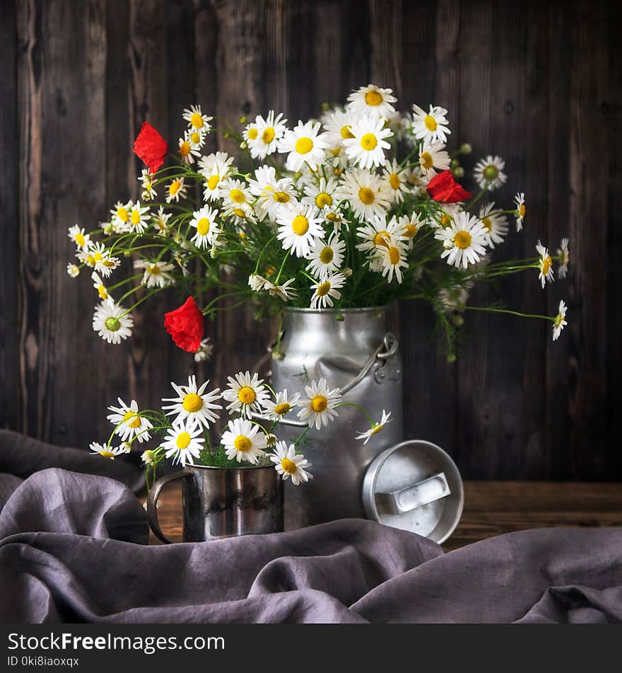 Rustic Still Life. Bouquet chamomile flowers and poppies in a metal can on a wooden background