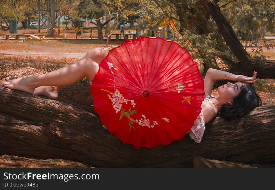 Woman Laying On Tree Log Holding Red Umbrella