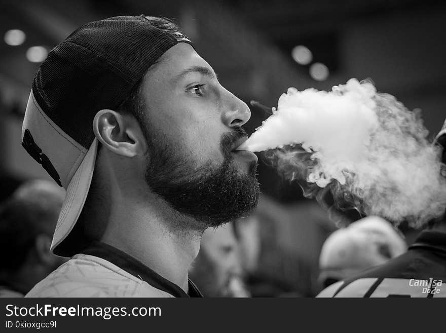 Grayscale Photography of Man Wearing Cap With Smoke on Mouth