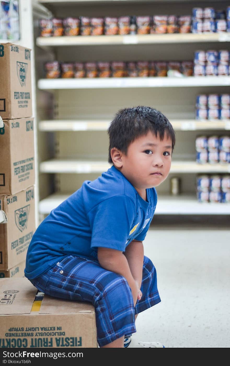 Boy Wearing Blue Crew-neck T-shirt Sitting on Cardboard Box